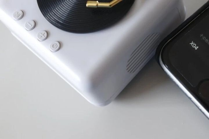 白いレコードプレーヤー型スピーカーの横にスマートフォンが置かれ、Bluetooth接続画面が見える