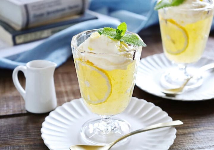 脚付きグラスに盛った黄色いとろぷるわらび餅とレモンクリームに、輪切りレモンとミントを飾った写真
