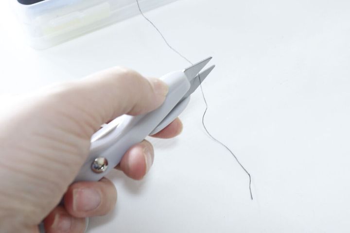 白い「指通し付にぎりハサミ」で黒い糸を切っている様子