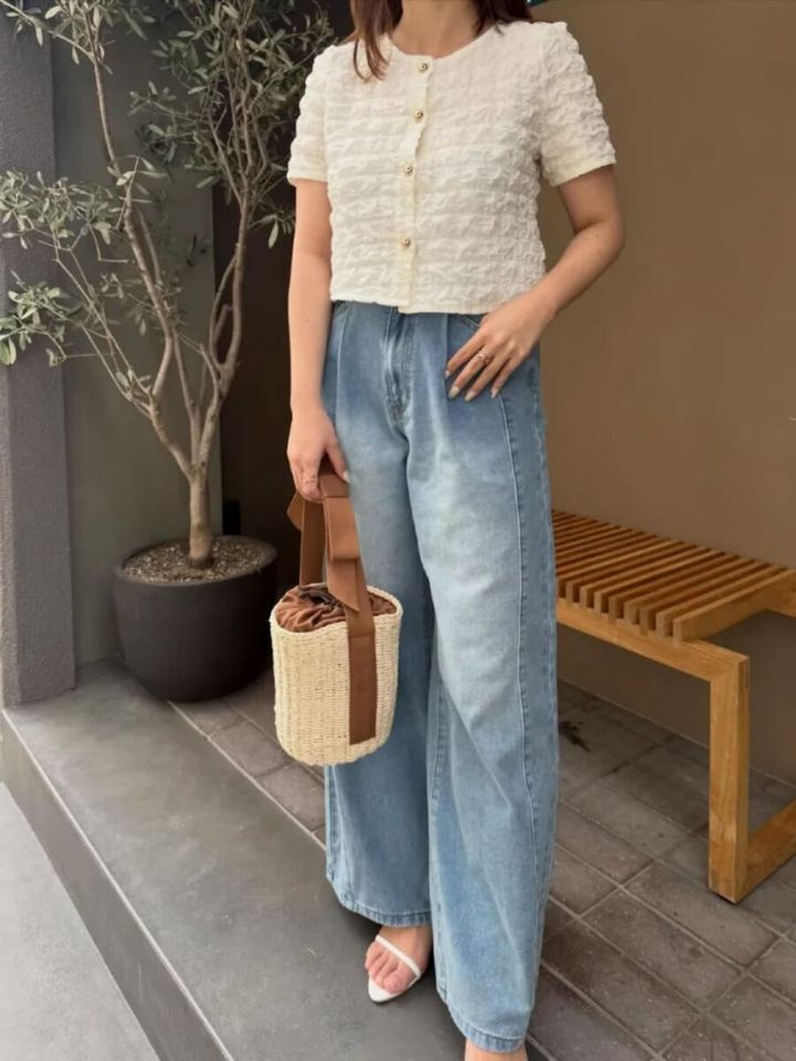 白のショート丈カーデとワイドデニムを着用しカゴバッグを持つ女性