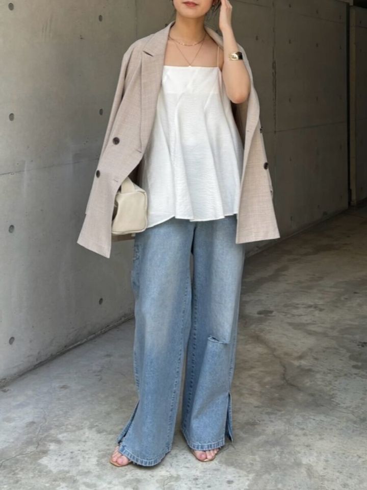 白キャミとワイドデニムにベージュジャケットを肩掛けする女性