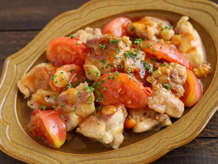 茶色い楕円形の器に盛られた、つやのあるガリバタソースをまとった鶏肉とトマトのガリバタ炒めのアップ写真