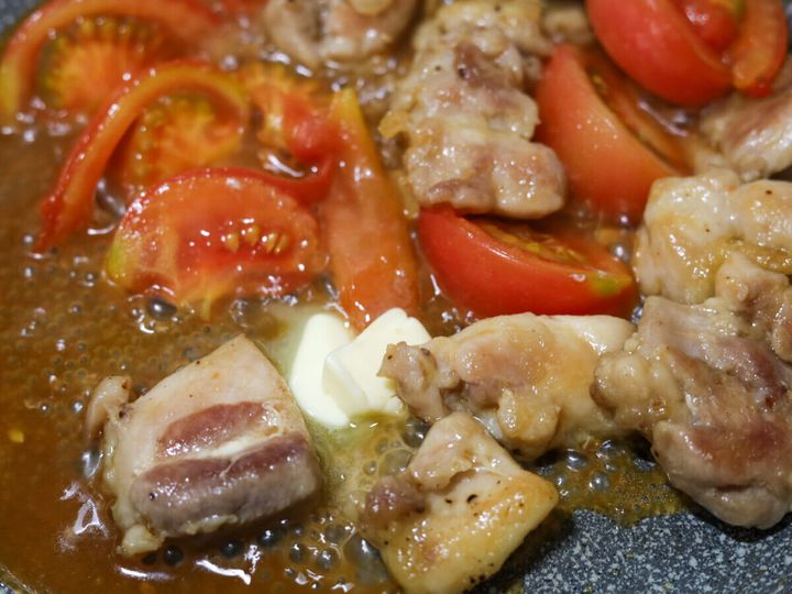 鶏もも肉とトマトを炒め合わせたフライパンにバターのかたまりを加えて溶かし絡めている様子