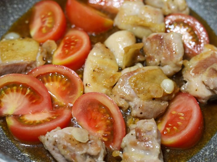 焼いた鶏もも肉にくし切りトマトと合わせ調味料を加えて炒め合わせている様子