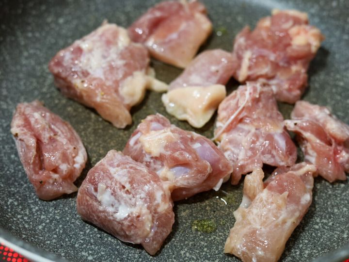 グレーのフライパンに片栗粉をまぶした鶏もも肉を皮目から並べて焼きはじめた様子