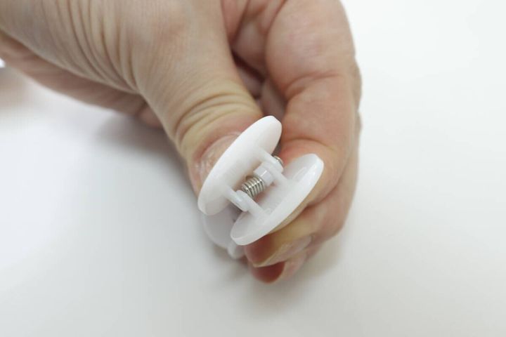 指で白いクリップを開き、内部のバネが見えている