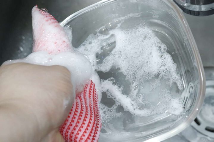 赤いスポンジでガラス容器を泡立てて洗っている様子