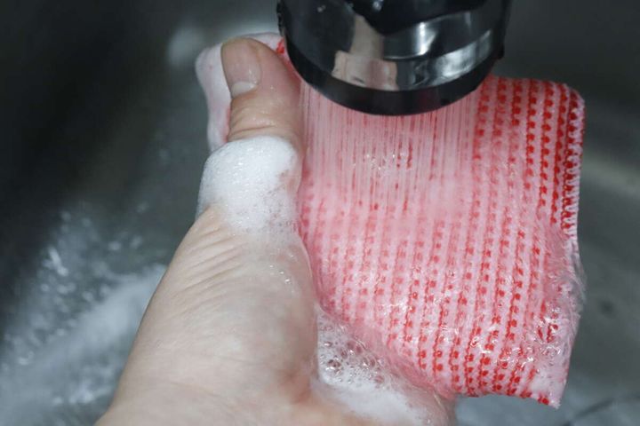 蛇口から流れる水で泡を洗い流している赤いスポンジ