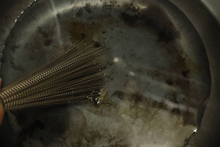 汚れたフライパンの底を中華鍋用ステンレスブラシでこすっている