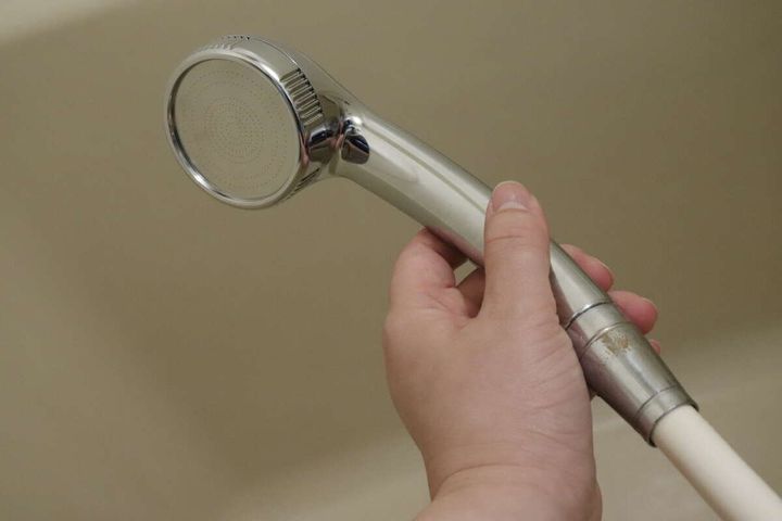 浴室でシャワーヘッドを手に持ち、ホースに接続している様子