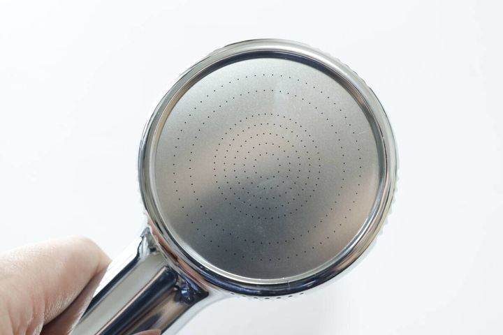シャワーヘッドの散水板部分を指で持っているクローズアップ