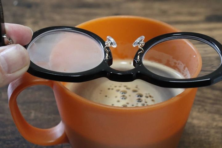 黒縁メガネを湯気の立つホットコーヒーのカップにかざしている様子