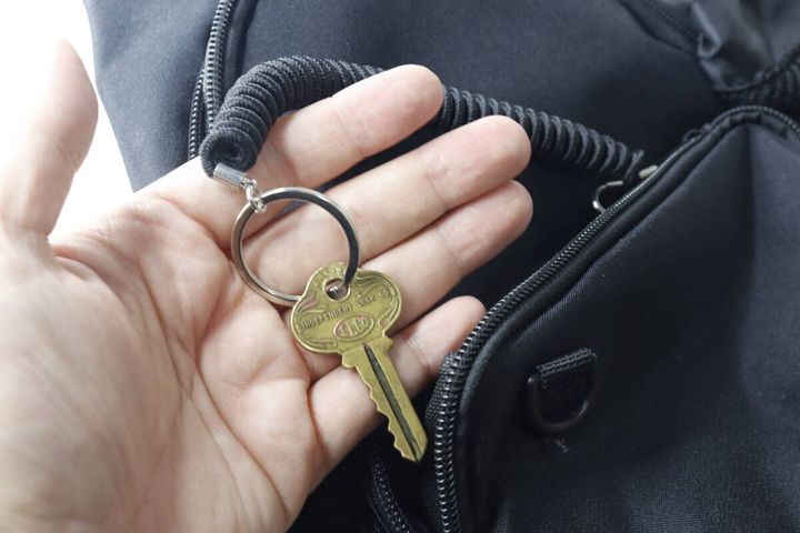 黒いバッグのファスナーからスプリングキーホルダーで繋がった鍵を取り出す手
