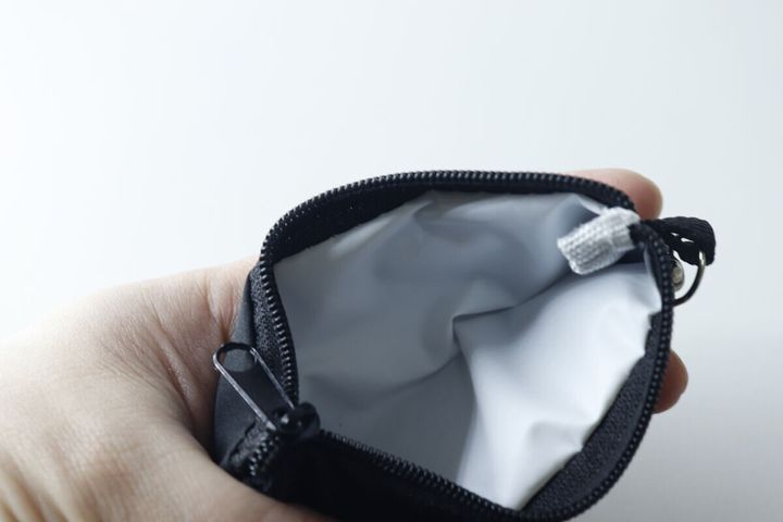 手のひらで開かれた黒いミニポーチ。内側の白いビニール素材が見える。