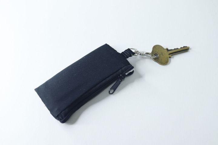 白い背景に置かれた黒いミニポーチ。フックに鍵が一つ付いている。