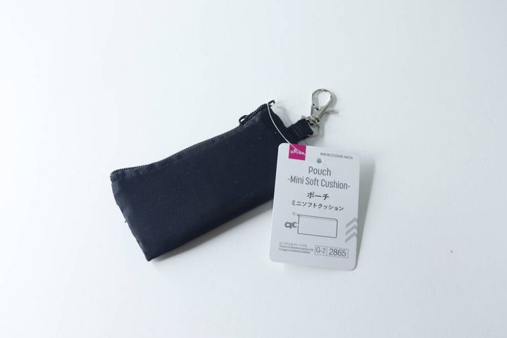 白い背景に置かれた黒いミニポーチ。商品タグが付いている。