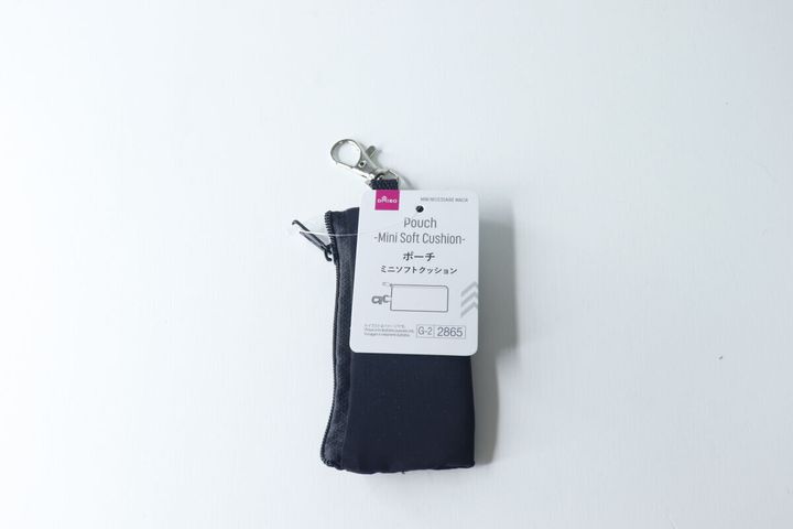 白い背景に置かれた黒いミニポーチ。商品タグが付いている。