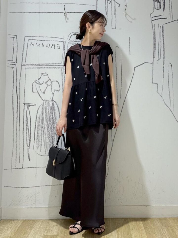 黒刺繍ペプラムニットと茶サテンスカートの女性が肩掛けカーデで横を向く
