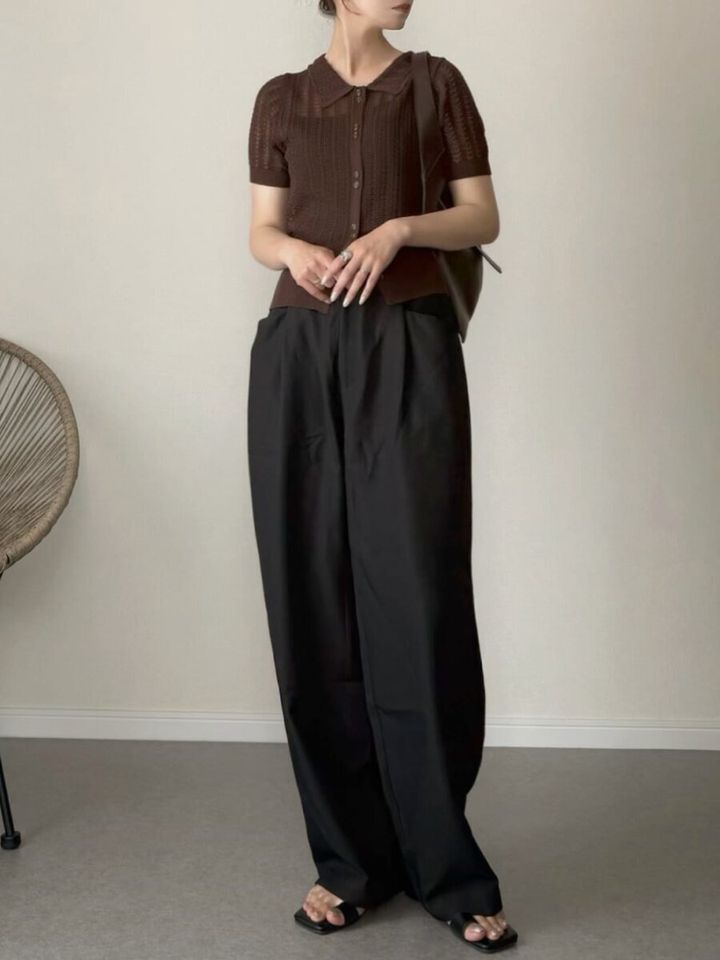 茶色襟付きシアーニットと黒ワイドパンツの女性が両手を組み下を向く