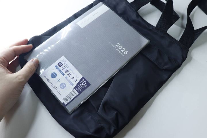 黒い2WAYショルダーバッグにA5サイズのスケジュール帳を入れようとしている手