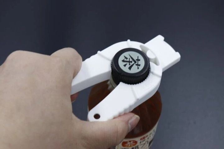 白い多機能オープナーで茶色い液体の入った瓶の黒いキャップを回している手元