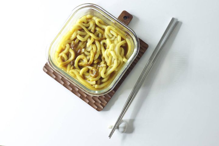 透明な耐熱容器に入ったカレーうどんと、横に置かれた箸