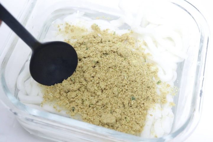 透明な耐熱容器に入れたうどん麺に粉末スープを入れ、スプーンを添えている