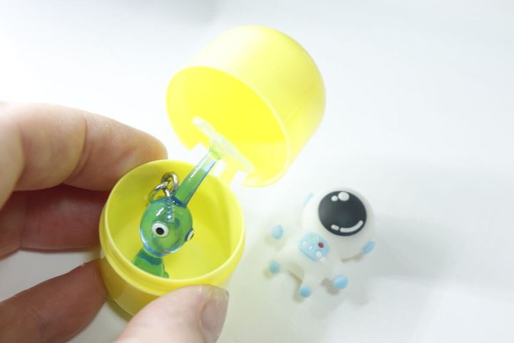 黄色いカプセルから宇宙飛行士と緑のエイリアンのマスコットが出てきた様子