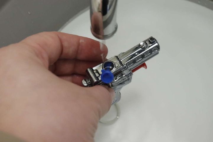 蛇口の下で水鉄砲キーホルダーの青いキャップを開け水を補充する手