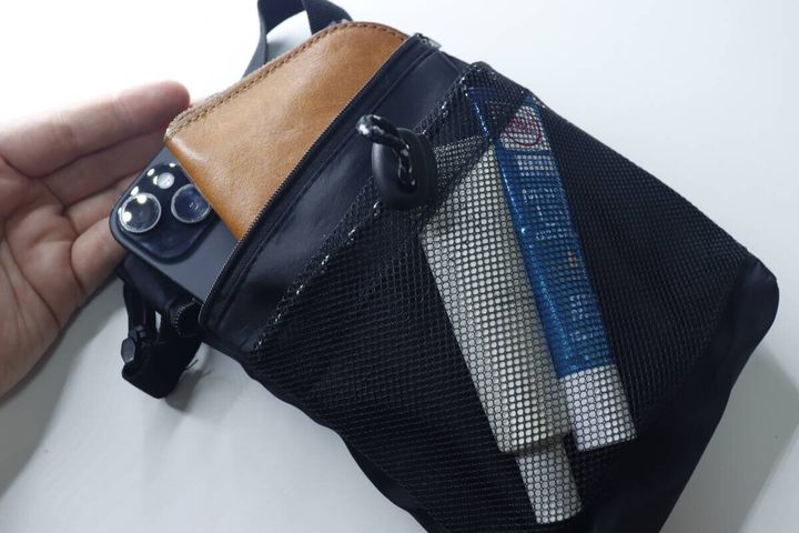 黒いバッグのポケットにスマホ、茶色い折財布、ハンドクリームを入れている