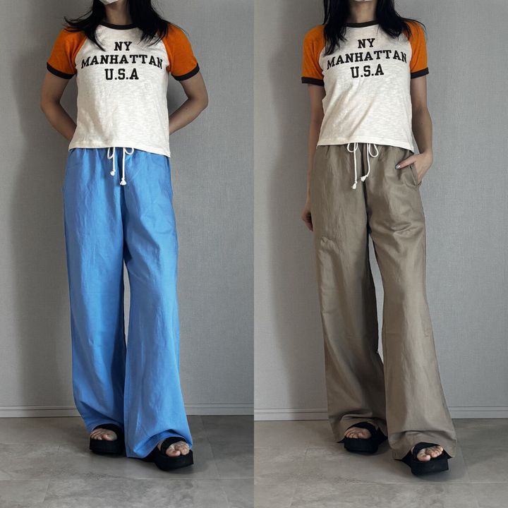 白とオレンジのロゴTシャツとブルー・ベージュパンツを履いた女性