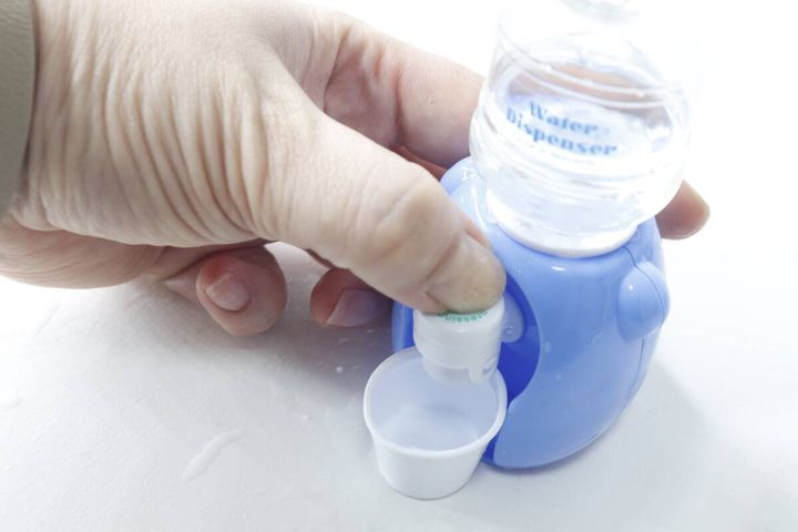 手でミニウォーターサーバーのボタンを押しコップに水を出している