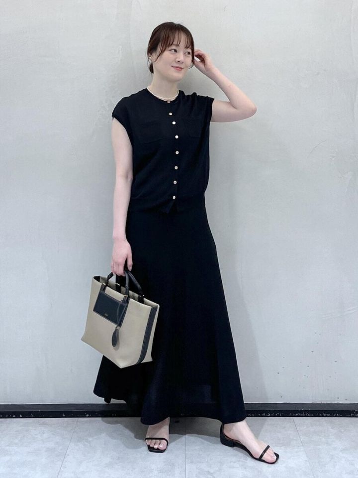 黒いニットとロングスカートを着てベージュのバッグを持つ女性