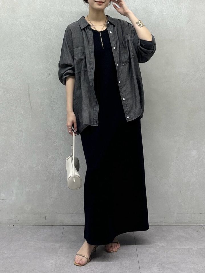 黒いワンピースにデニムシャツを羽織り白いバッグを持つ女性