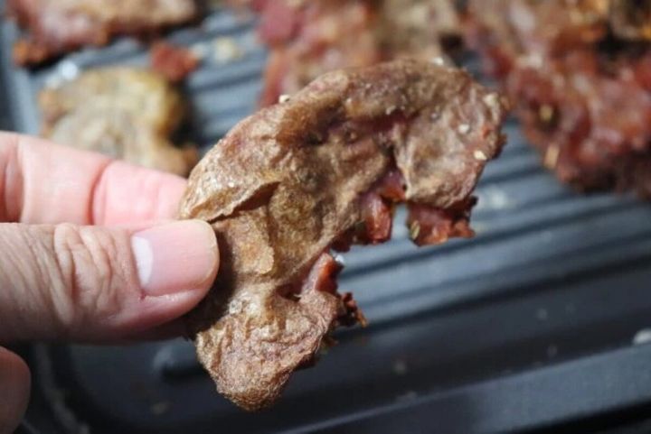 焼かれた肉片を指でつまんで持ち上げている手元