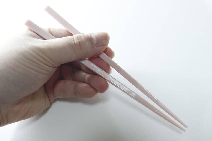 右手がピンク色の箸を持ち、先端の滑り止め部分が見える