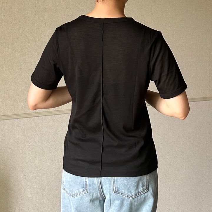 黒いシアーTシャツと薄いブルーのデニムパンツを着用した女性が後ろを向いて立っている