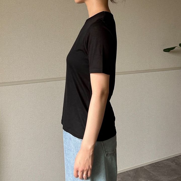 黒いシアーTシャツと薄いブルーのデニムパンツを着用した女性が横向きに立っている