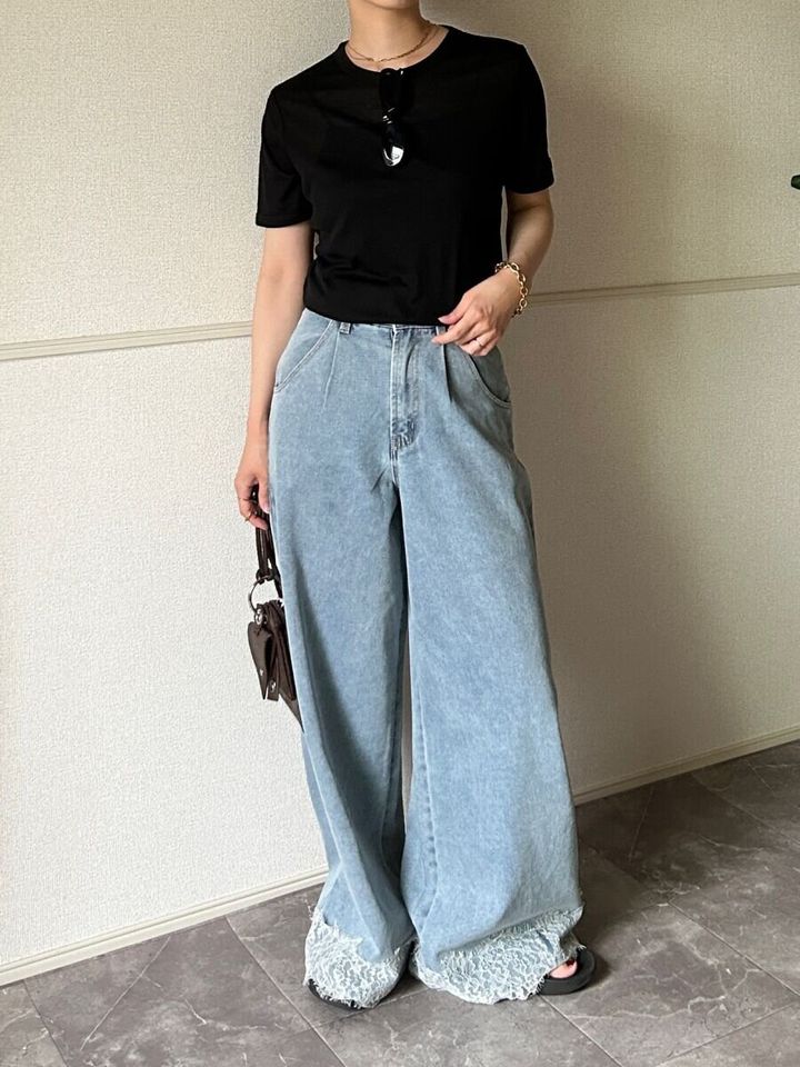 黒いシアーTシャツとデニムパンツを着用した女性がサングラスを胸元にかけバッグを持って立っている