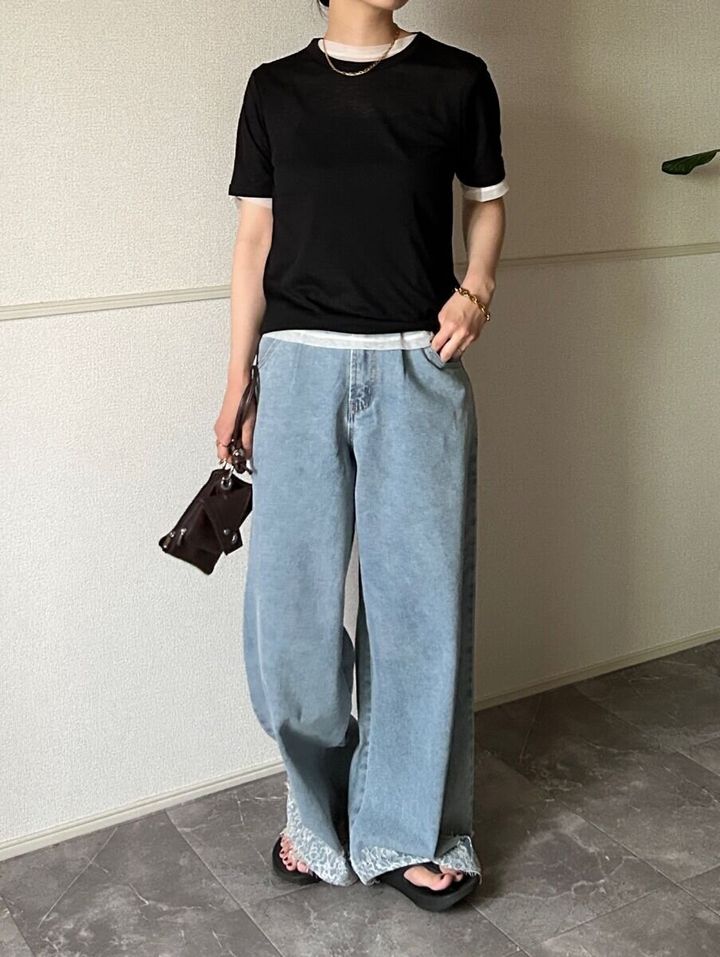 黒いシアーTシャツの下に白いTシャツをレイヤードしデニムパンツを着用した女性が立っている