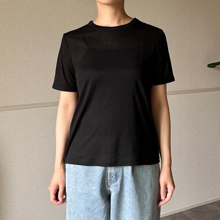 黒いシアーTシャツと薄いブルーのデニムパンツを着用した女性が正面を向いて立っている