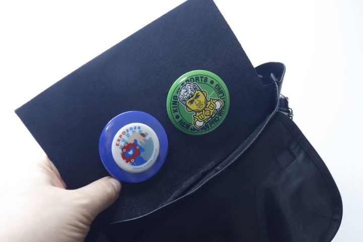 黒い中敷き台紙に青と緑の缶バッジを取り付けている手元