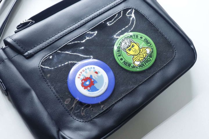 黒いバッグのクリア窓から見える青と緑の缶バッジ
