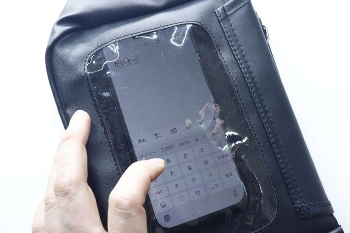 黒いバッグのクリア窓越しにスマートフォンを指で操作している