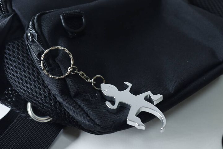 黒いバッグのファスナーに、銀色のトカゲ型栓抜きキーホルダーが付けられている