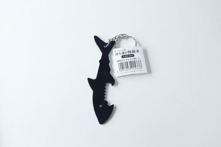 黒いサメ型栓抜きキーホルダーが白い背景に置かれ、商品タグが付いている