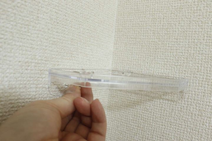 白い壁のコーナーにクリアコーナーラックを取り付けている手元