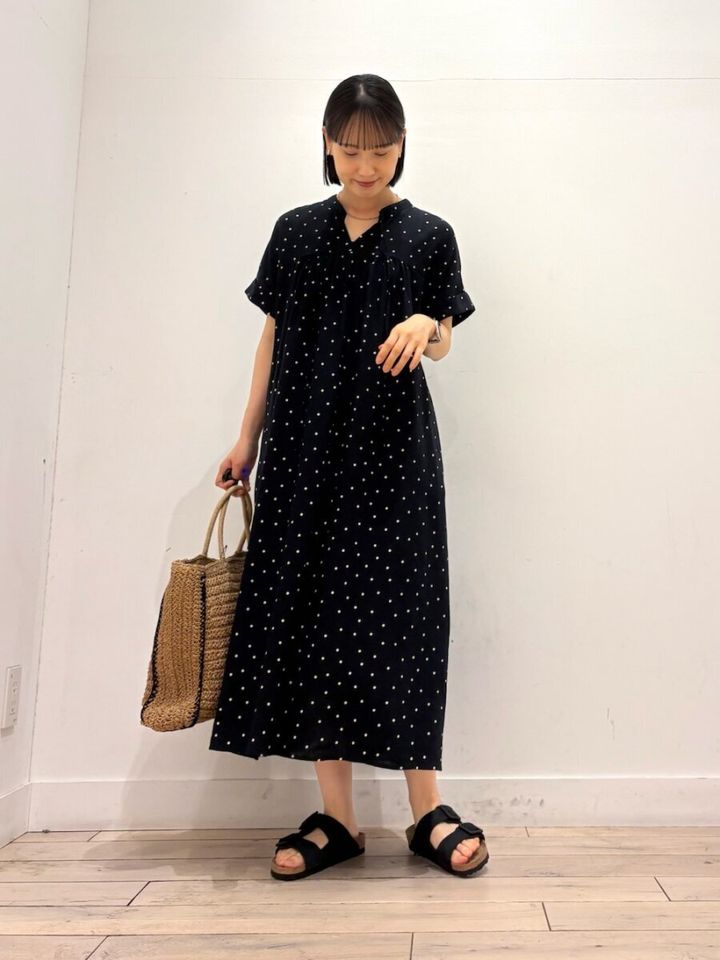 ドット柄黒ワンピースの女性が、かごバッグを持ち下を向いて微笑む