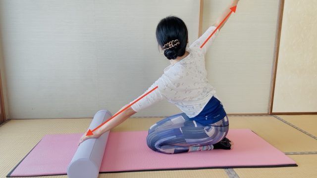 正座で片手をポールに置き、反対の腕を斜め上に伸ばして胸を開く女性