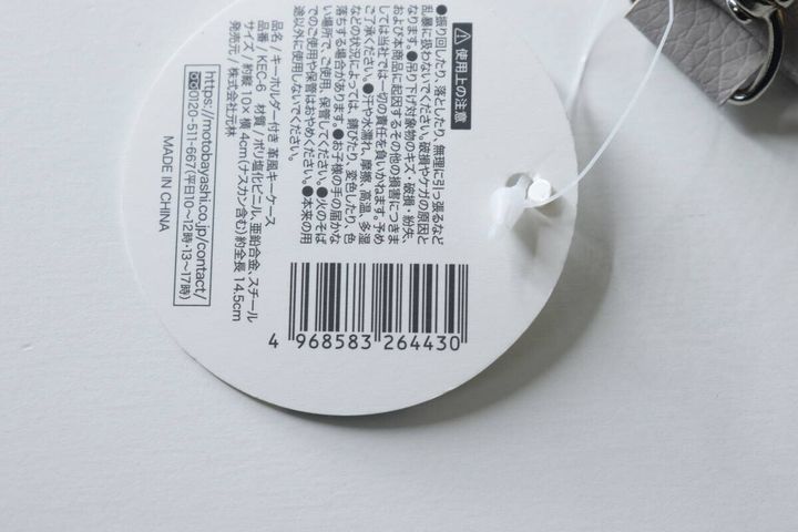 グレーの革風キーケースに付いている商品タグの裏面、JANコードや注意書きが写っている